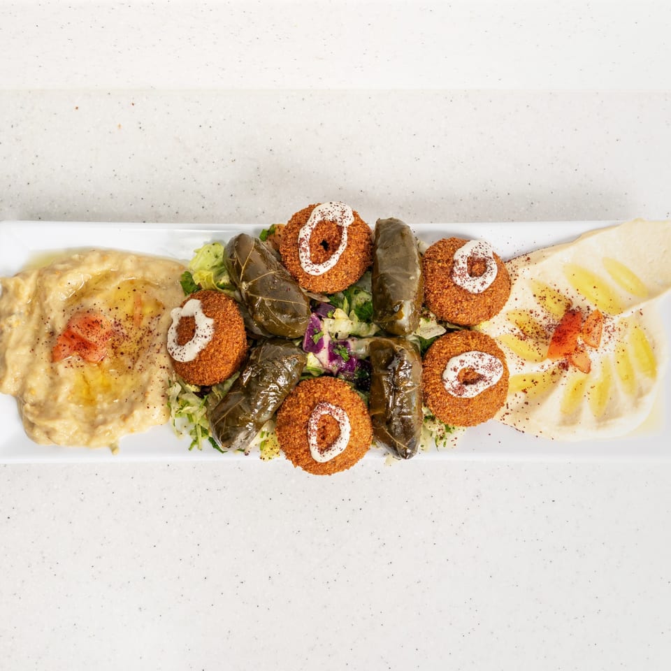 A white platter with falafel, stuffed grape leaves, baba ghanoush, and hummus.