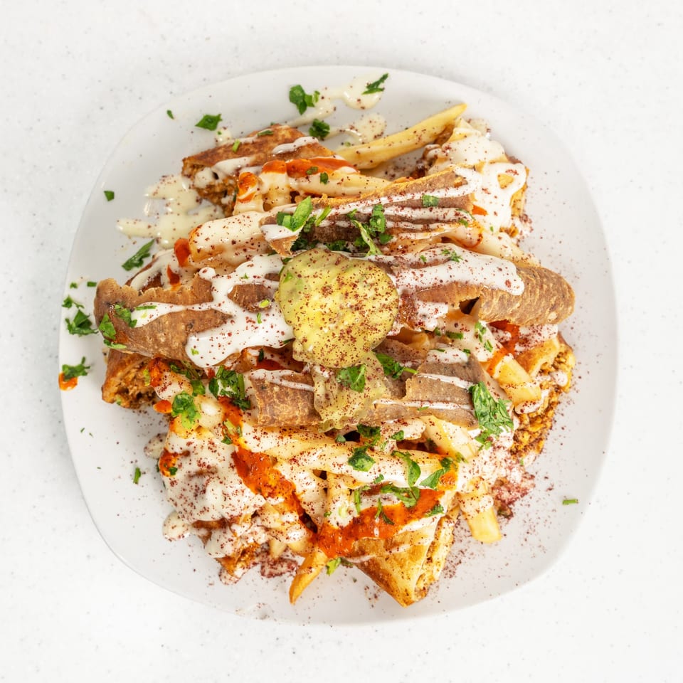 A white plate piled high with fries, meat, sauces, and herbs, viewed from above.